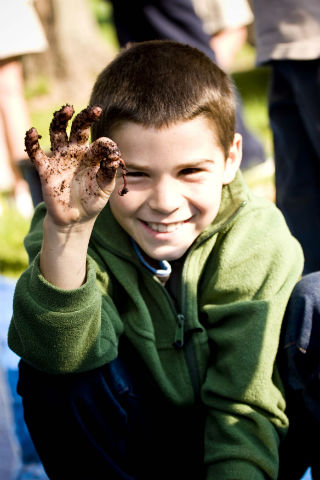 Boy with dirt covered hands holding an earthworm.