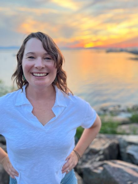 A woman smiles at the camera on a rocky beach