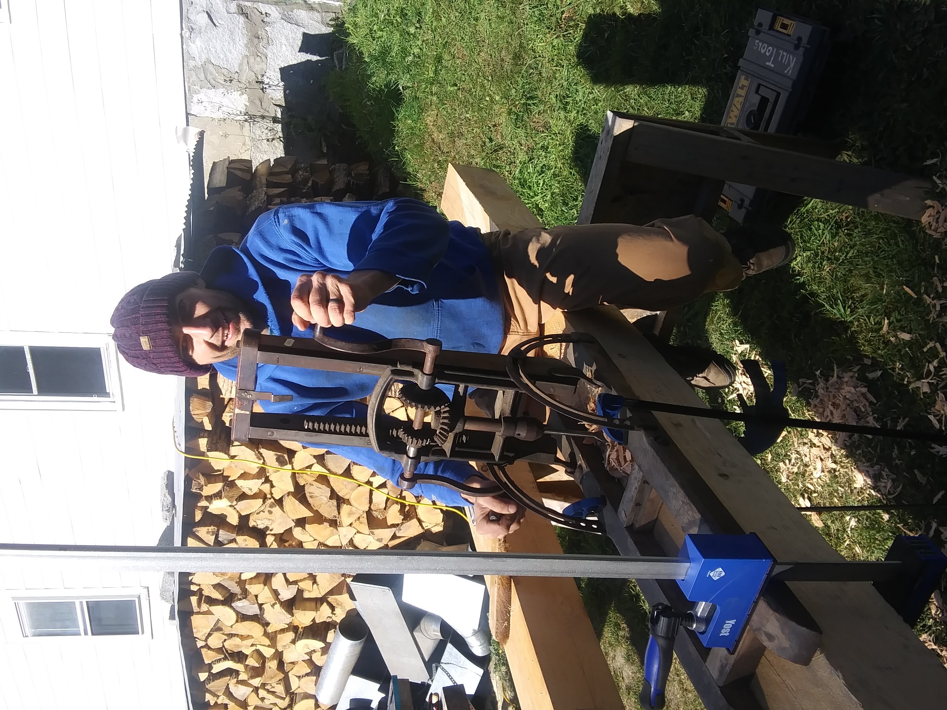 A man in a blue hoodie stands behind woodworking equipment