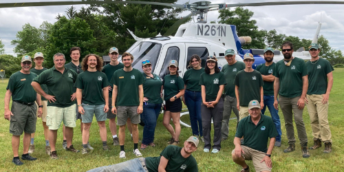 A group of smiling park staff pose in front of a helicopter on Burton Island