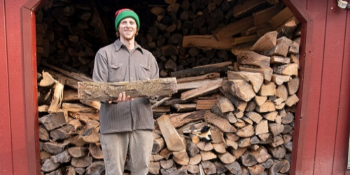 Smiling man standing in front of a stack of wood.