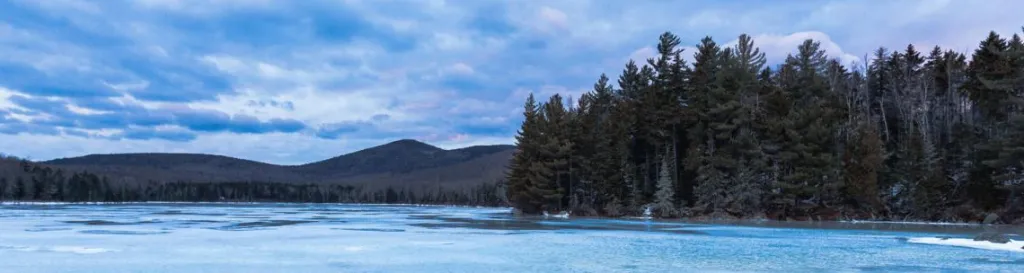 A wintery view of Noyes Pond at Seyon Lodge shows blues and purples in the horizon and a partially frozen lake.